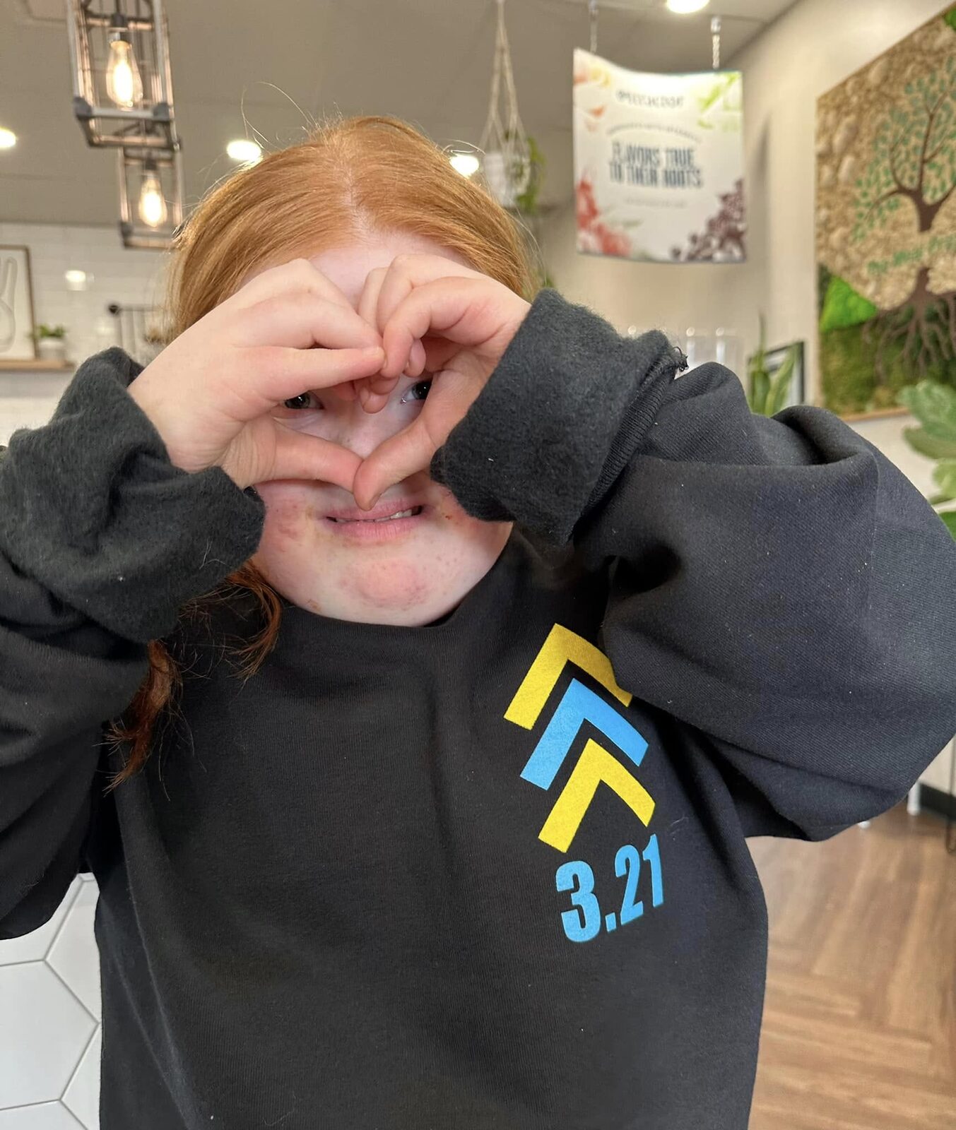 A girl in the 3.21 sweatshirt making a heart with her hands