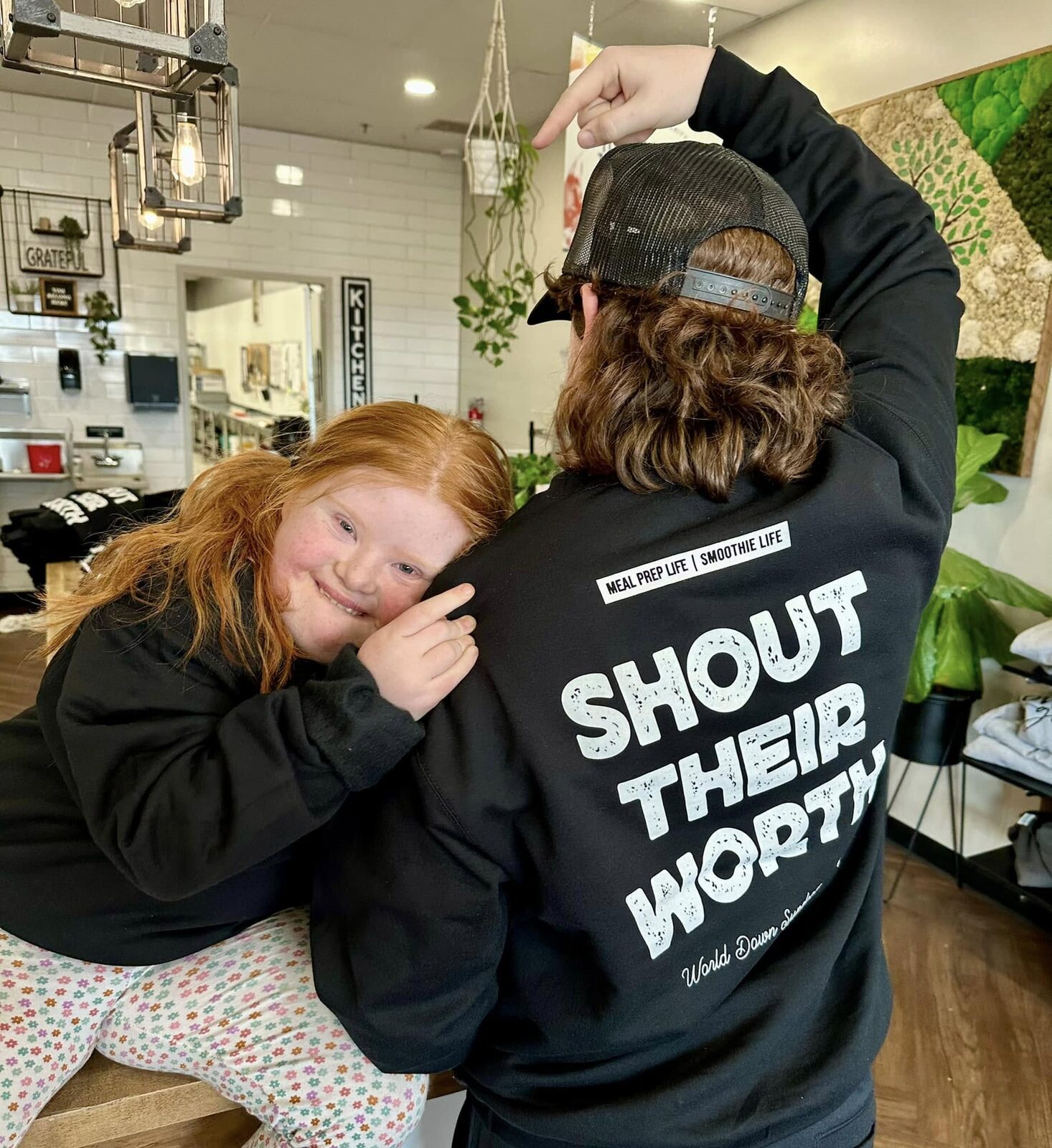 A girl hugging one of the team, both in the Shout Their Worth shirts, on World Down Syndrome Day at the shop