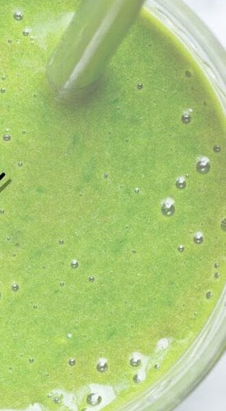A green smoothie in a glass with a spoon, from above