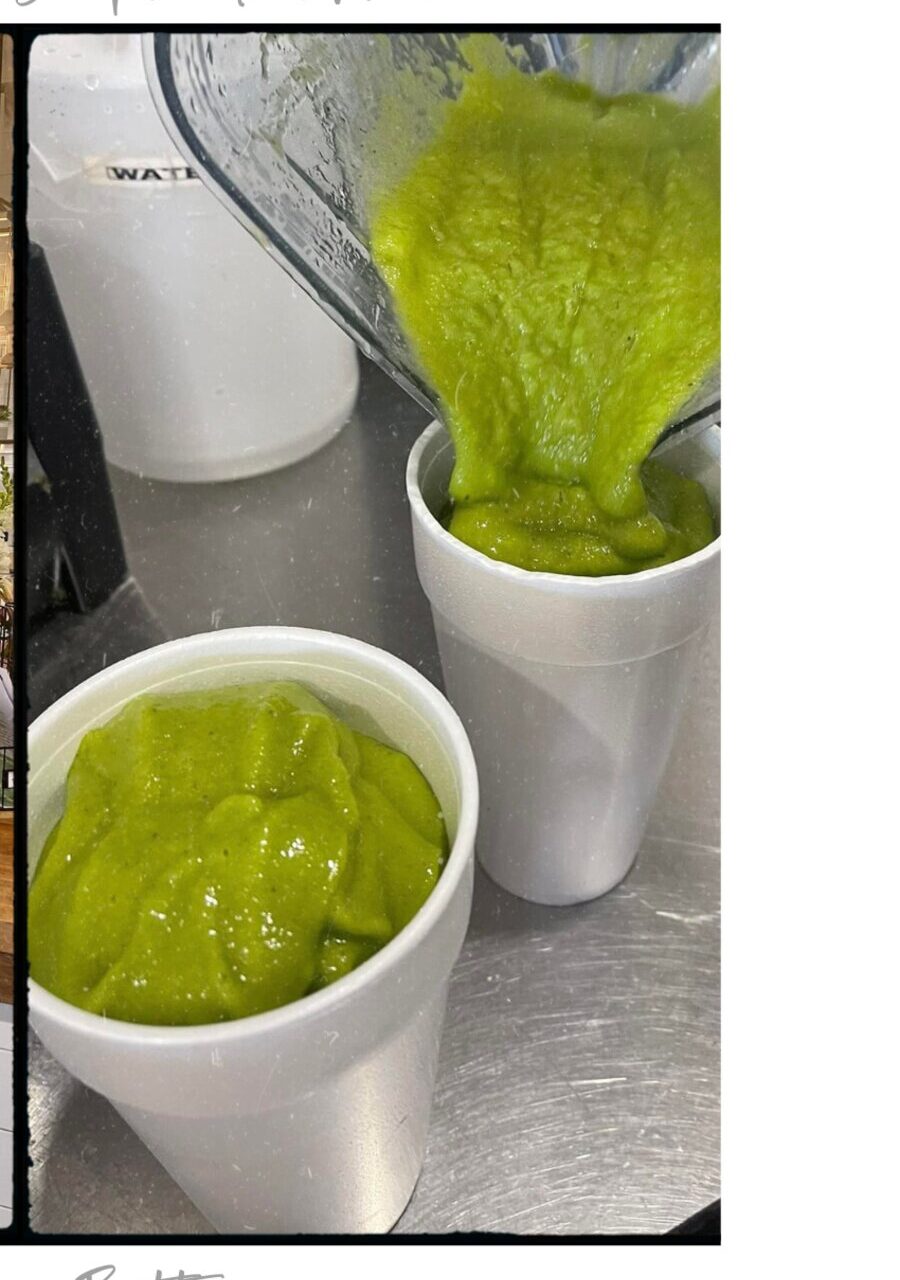 A thick green smoothie being poured from the blender into a cup