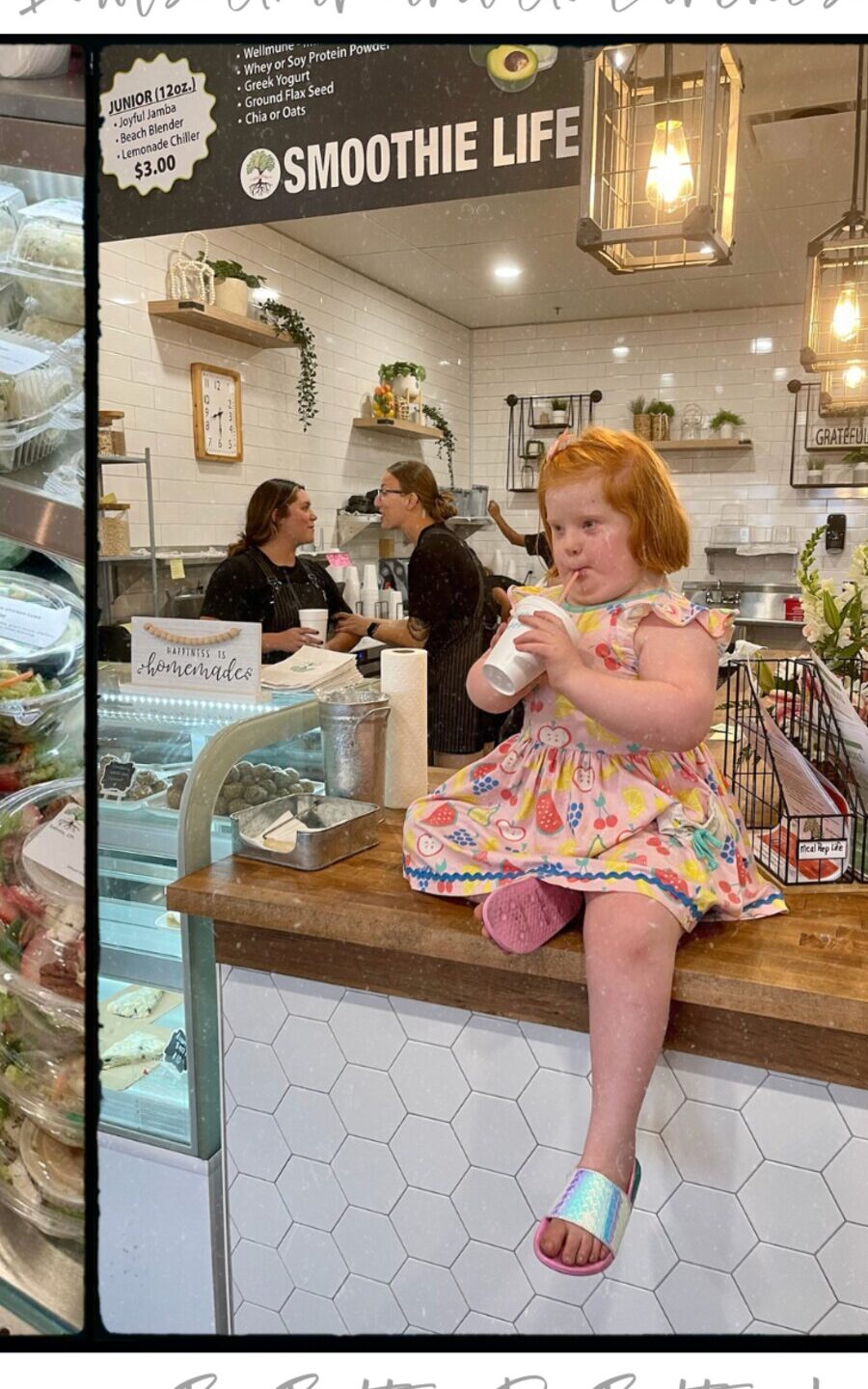 A little girl sitting on the counter with her cup, the team and the menu board behind her