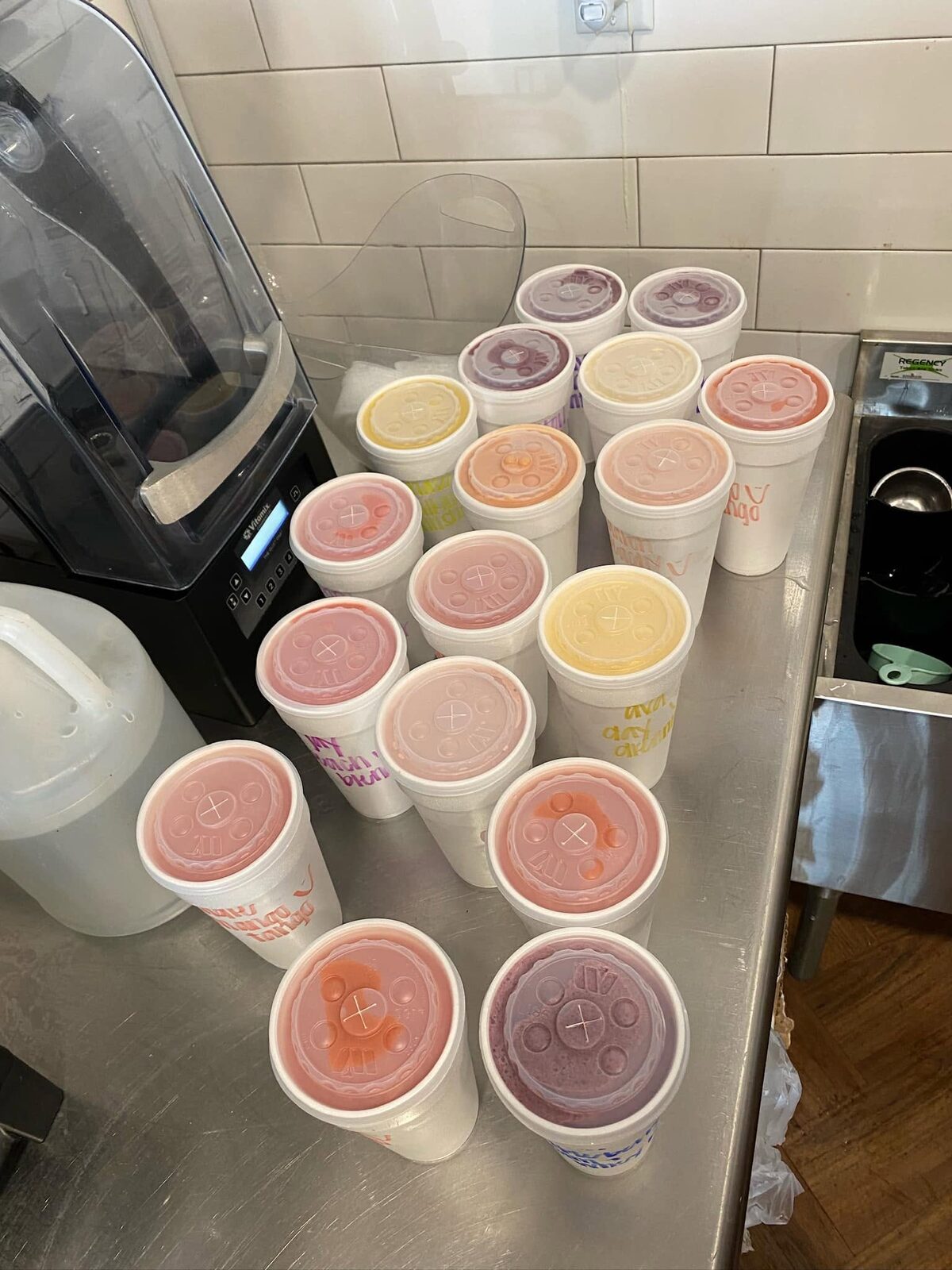Lidded smoothie cups in a row of colours beside the blender