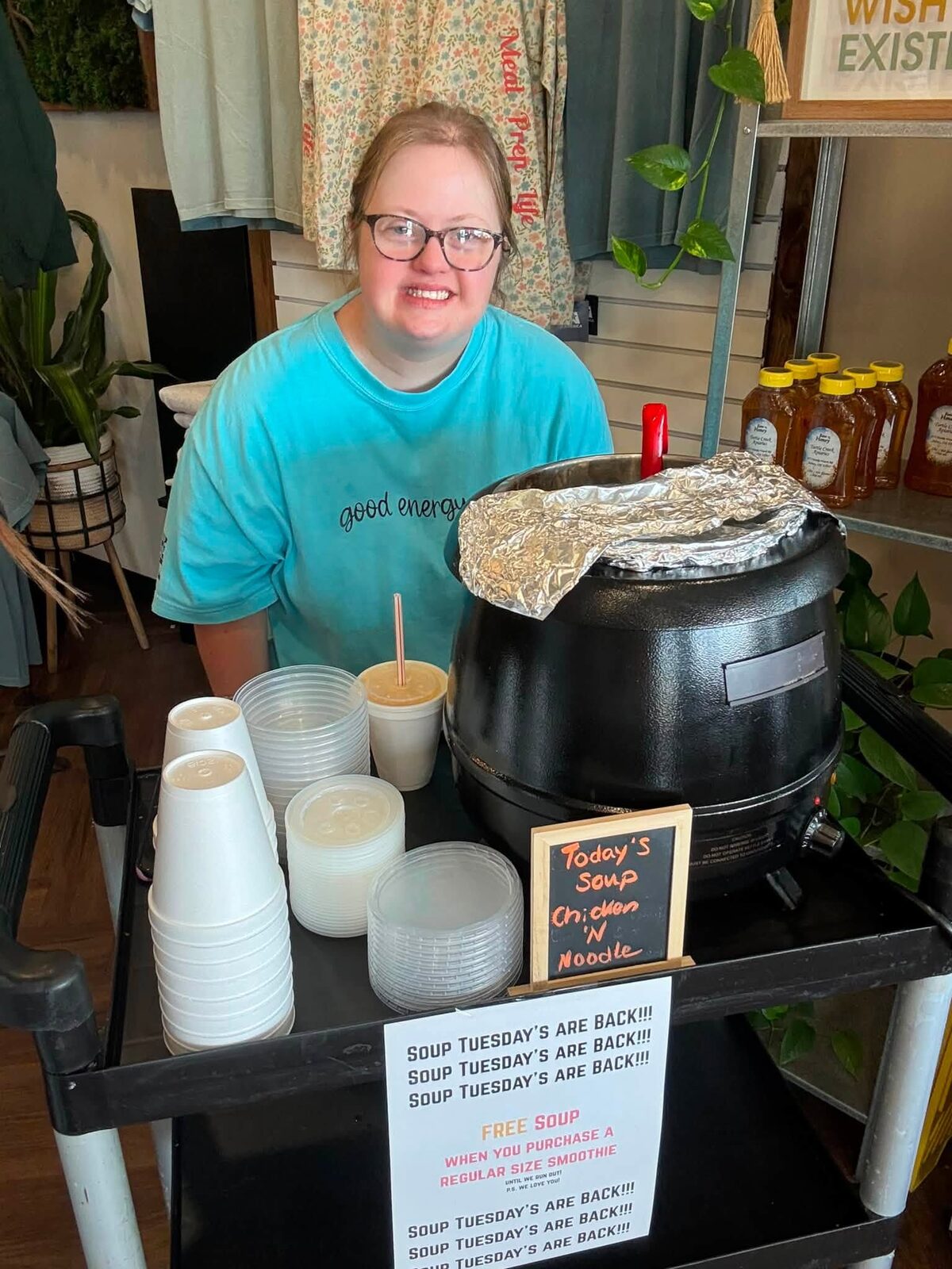 One of the team smiling at the soup station with the Soup Tuesday sign