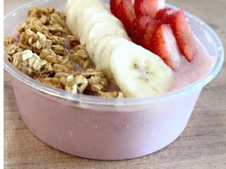 A pink smoothie bowl topped with sliced banana, strawberries and granola, at the shop
