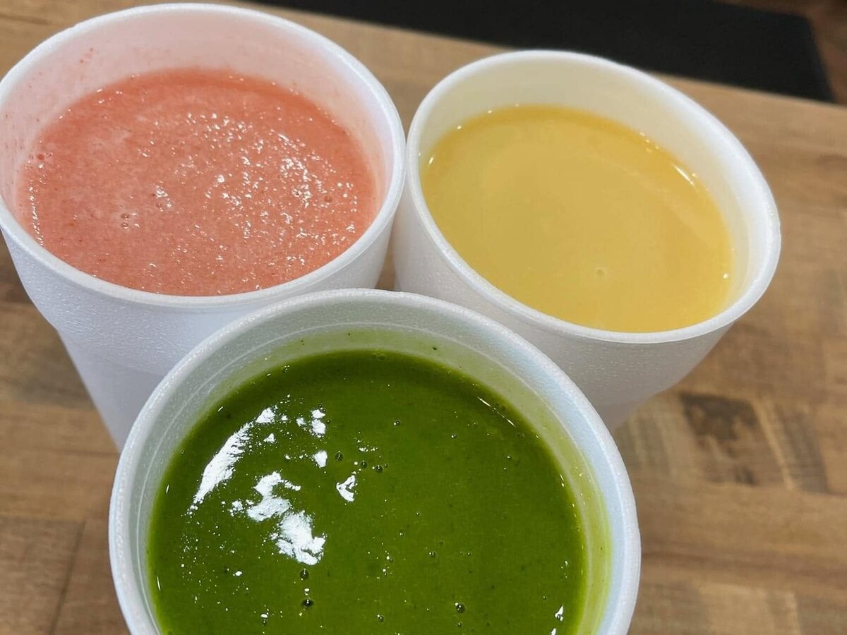 Three drinks in white cups on the wood counter — pink, green and yellow