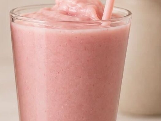 A pink strawberry smoothie in a tall glass with a straw, close up