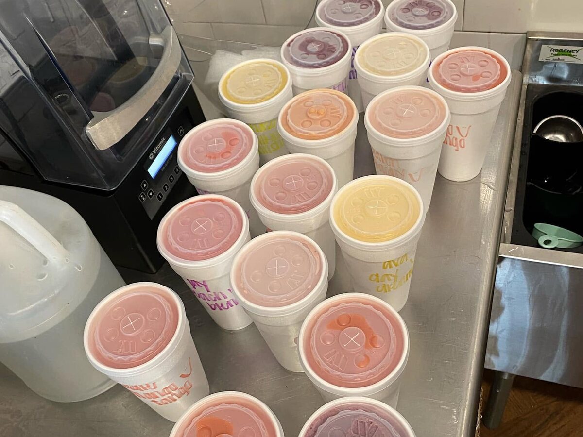 A tray of lidded smoothie cups in pinks, yellows and purples next to the blender at the shop