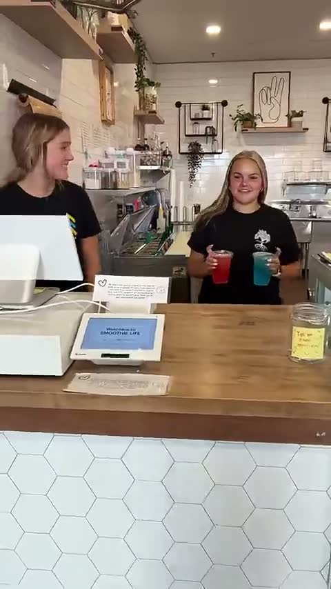 Two of the team at the counter holding a red and a blue drink — her reel: Smile, we love you