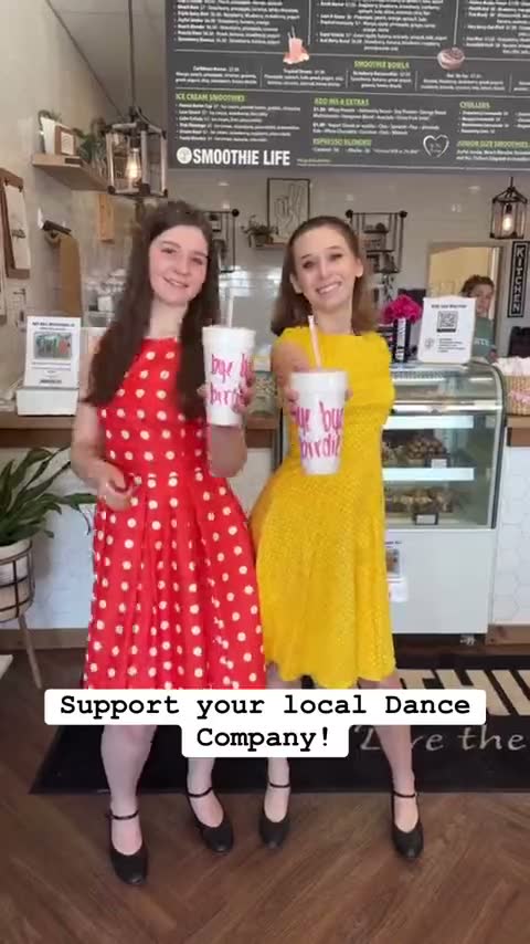 Two dancers in red and yellow dresses holding cups at the counter — her reel supporting the Sidney Dance Company